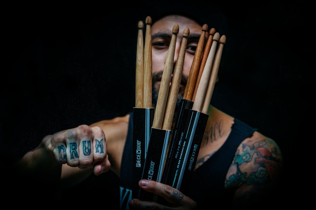 Musician showing drumsticks and tattoos, emphasizing creativity and style.