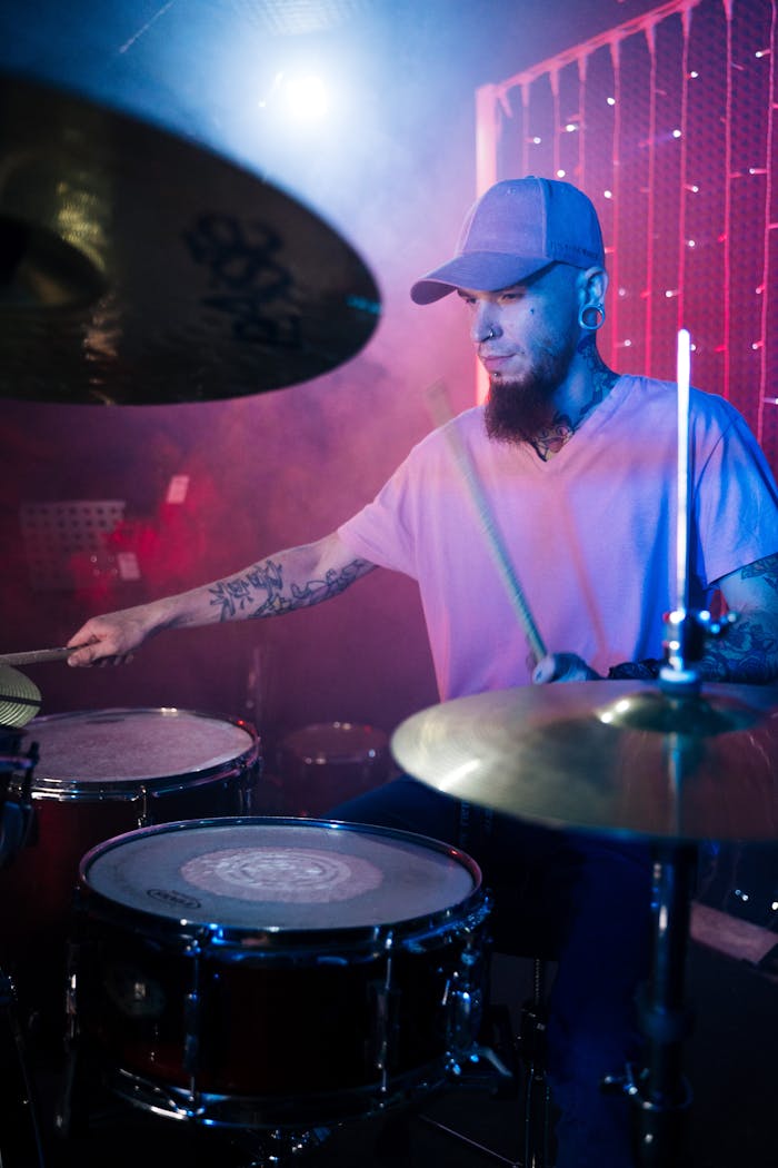 Tattooed drummer passionately playing drums in a vibrant stage performance.