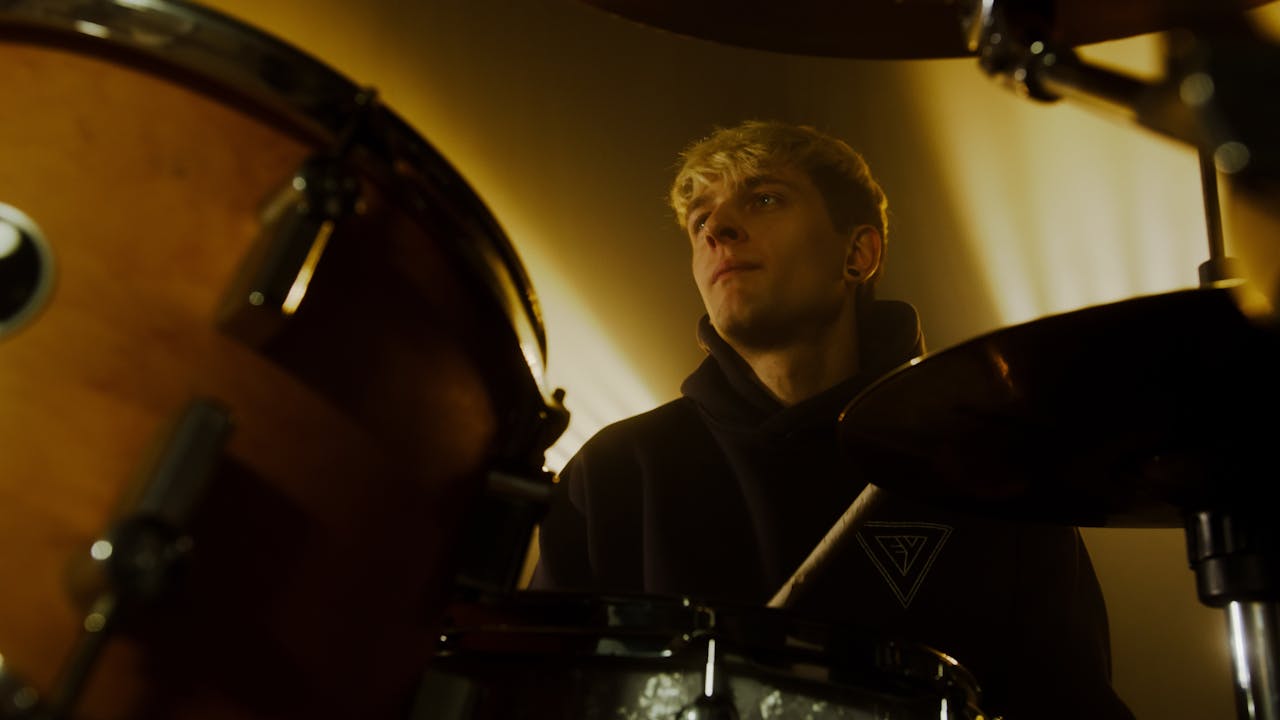 A young drummer immersed in his performance, playing the drums with a focused expression on stage.